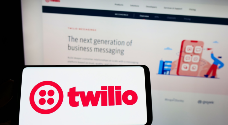 Person holding cellphone with logo of American communications platform company Twilio Inc. (TWLO) on screen in front of webpage. Focus on phone display. Unmodified photo.