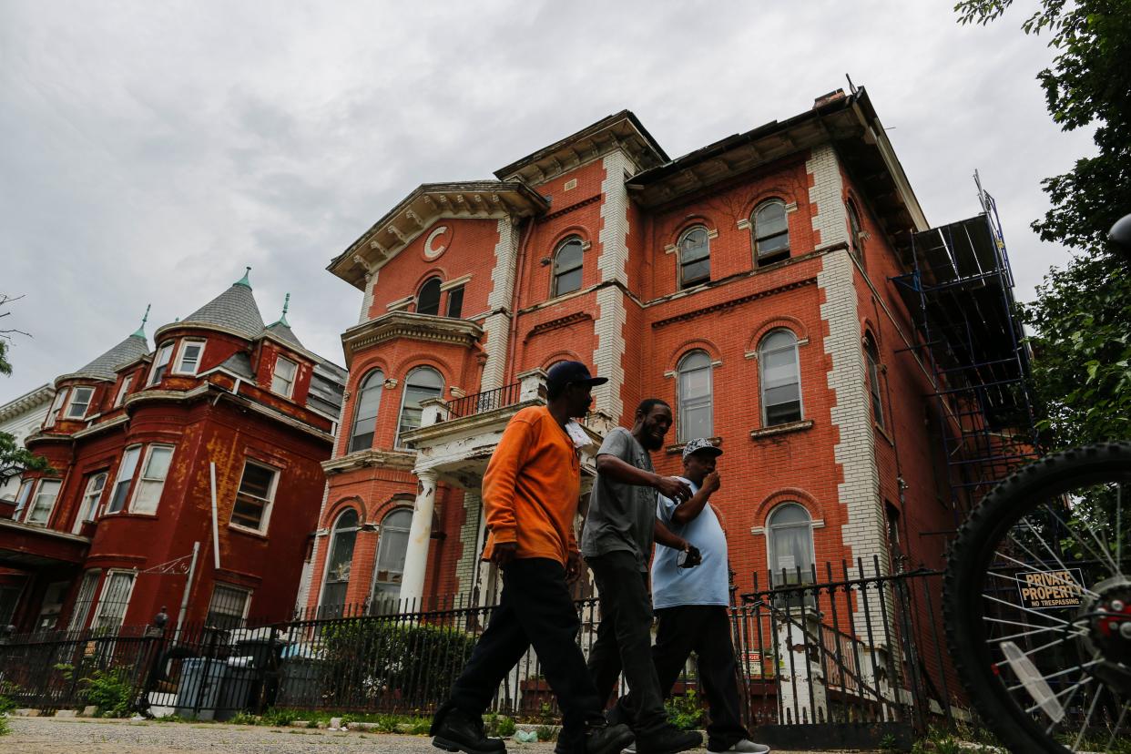 A man in a bright orange shirt and two friends pass a house painted a similar color.