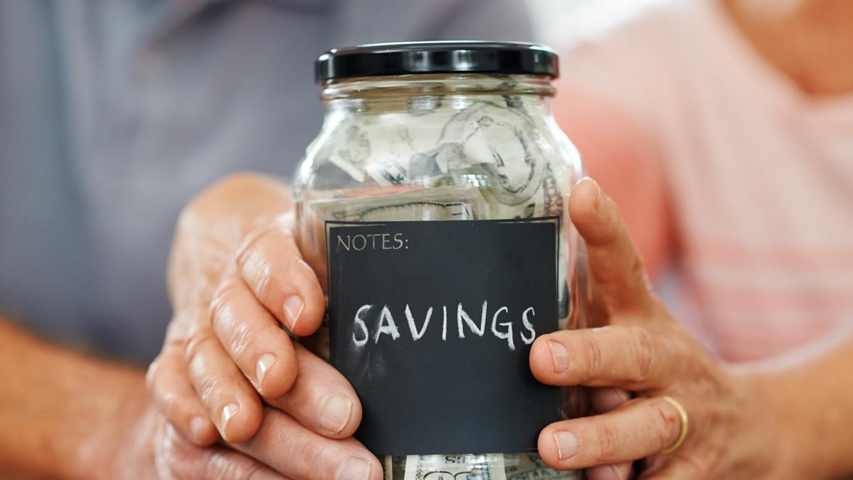 Shot of two pairs of hands wrapped around a mason jar of saved money.