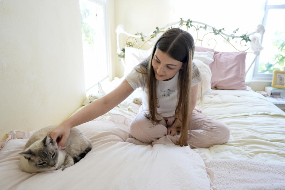 Amea Wadsworth pets her cat at her home, Friday, April 19, 2024, in San Diego. Wadsworth, who moved back home after graduating college, wanted to use her first full-time job as a chance to save, and a moment to take a hard look at her spending activity. (AP Photo/Gregory Bull)