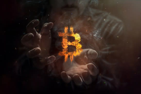 Burning symbol of bitcoin with a person's hands in the background.
