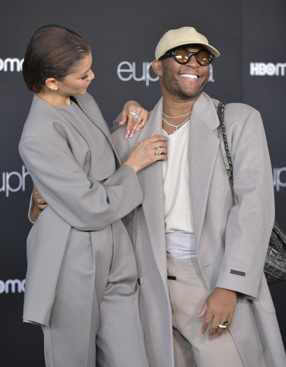 An image of Zendaya and Law in grey suits, smiling at a Euphoria event. Zendaya is affectionately arranging his lapel while he has his arm around her waist.