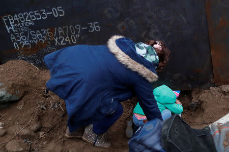 Maria Martinez and her daughter, Maria, 4, migrants from Honduras and part of a caravan of thousands from Central America trying to reach the United States, crawl through a hole under a border wall to cross illegally from Mexico to the U.S., in Tijuana, Mexico December 10, 2018. REUTERS/Carlos Garcia Rawlins