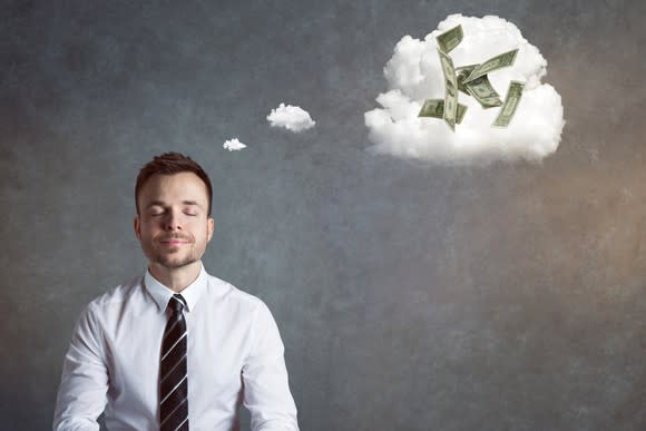 A man in a shirt and tie sits with money floating in a thought cloud above him.