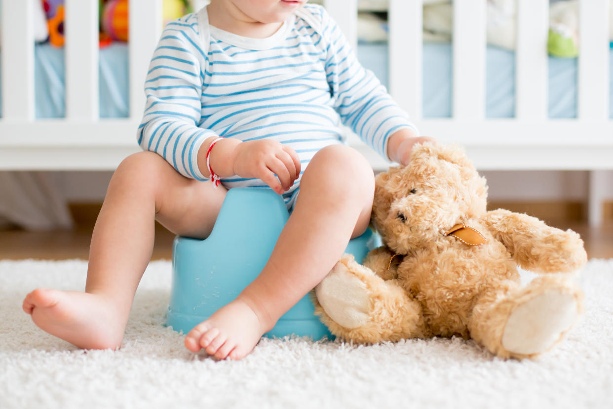 Cute toddler boy, potty training, playing with his teddy bear on potty