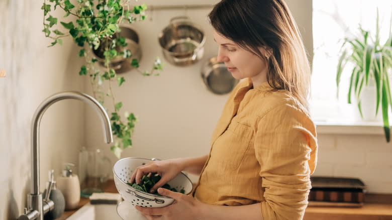 person rinsing spinach with colander 