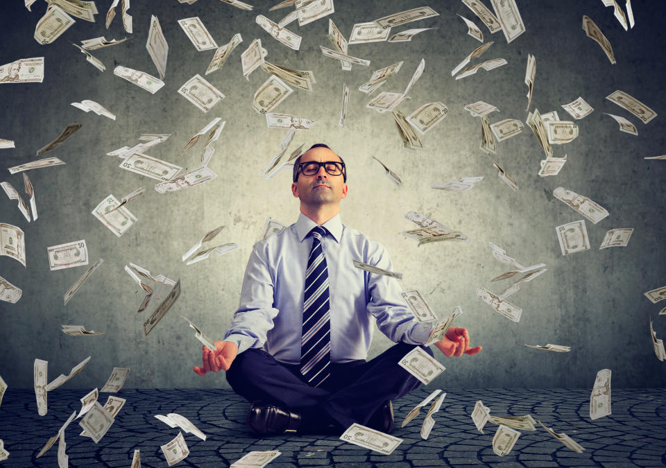 A man sitting in a yoga pose as $100 bills fall down around him.