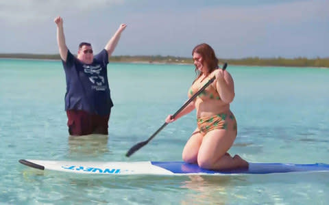 Steven (37 stone) cheers as plus size model Holly Macgillivray (20.5 stone) gets to grips with paddle boarding - Credit: ITV