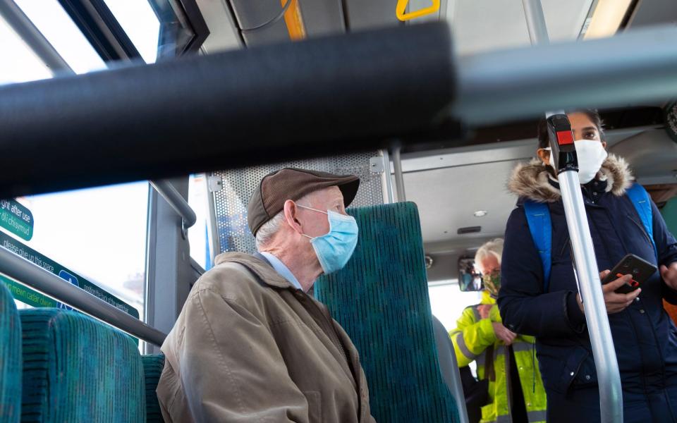 Elderly man passenger passengers wearing paper Covid mask pandemic masks sitting travelling on a bus in Cardiff Wales UK 2021 - Kathy deWitt / Alamy Stock Photo