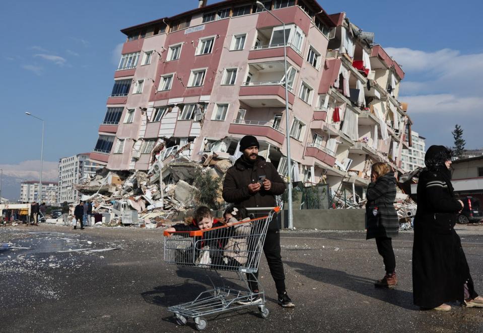 After: Children sit in a shopping cart near a collapsed building following an earthquake in Hatay, Turkey (Reuters)