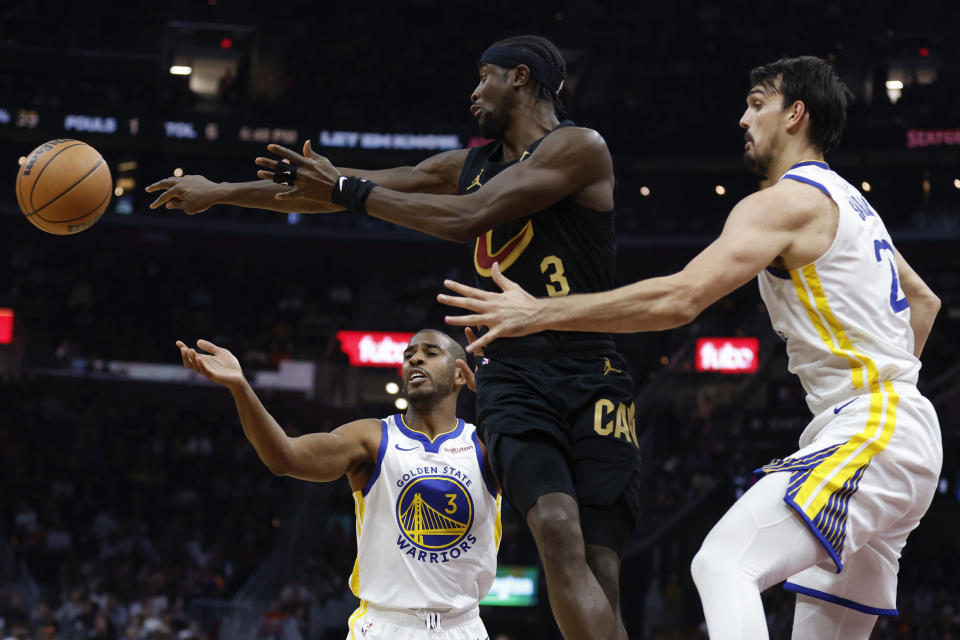Cleveland Cavaliers guard Caris LeVert, center, passes the ball against Golden State Warriors guard Chris Paul, left, and forward Dario Saric, right, during the first half of an NBA basketball game, Sunday, Nov. 5, 2023, in Cleveland. (AP Photo/Ron Schwane)