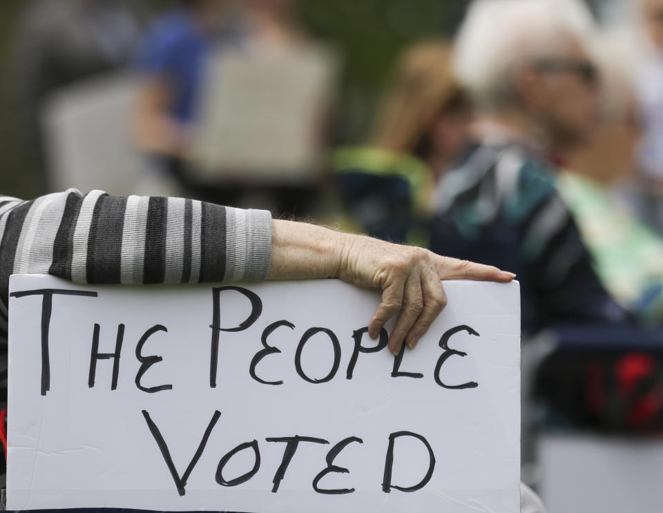 A rally attendee props up a sign with her hand while listening to speakers at the Tuesday, April 27, 2021, Medicaid expansion rally at the Missouri State Capitol in Jefferson City. The Missouri Legislature is the latest statehouse fighting to undo voter-backed ballot measures. Missouri's GOP-led Senate this week voted against paying for voter-approved Medicaid expansion. (Liv Paggiarino/The Jefferson City News-Tribune via AP)