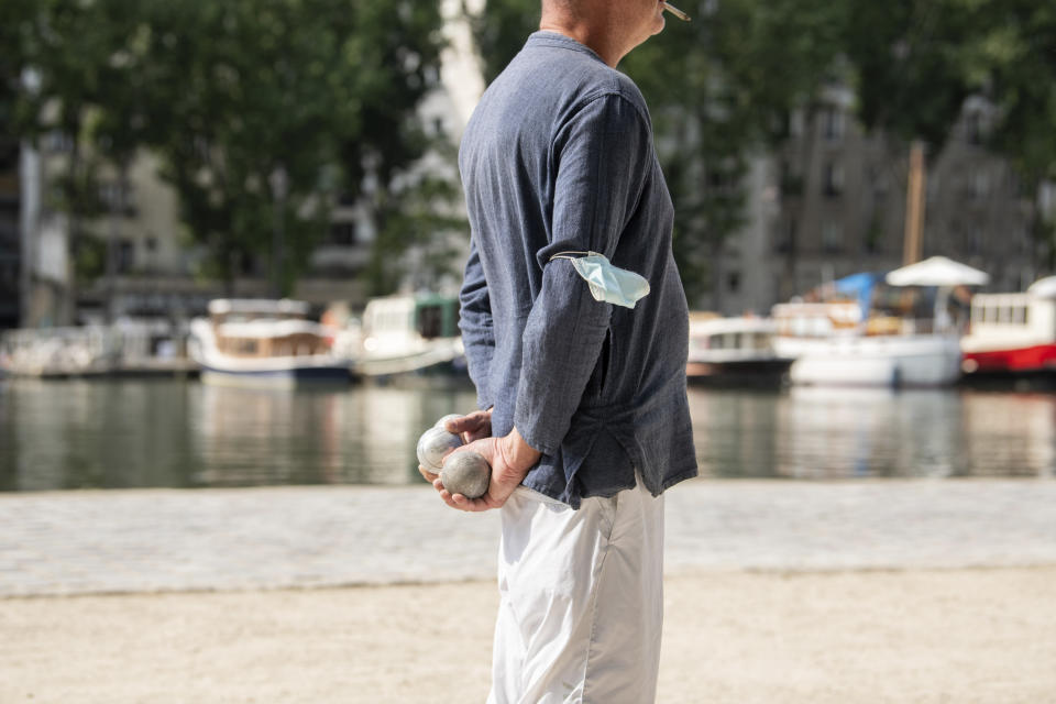 A man plays pétanque with his mask attached to his arm Wednesday, June 16, 2021 along the Canal de l'Ourcq in Paris. France on Wednesday eased several COVID-19 restrictions, with authorities saying it's no longer always mandatory to wear masks outdoors, and halting an 8-month nightly coronavirus curfew this weekend. (AP Photo/Benjamin Girette)