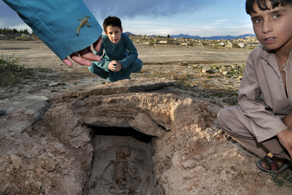 Afghan boys spend their time next to a destroyed grave at a cemetery in Kabul, Afghanistan, Thursday, May 5, 2022. There are cemeteries all over Afghanistan's capital, Kabul, many of them filled with the dead from the country's decades of war. They are incorporated casually into Afghans' lives. They provide open spaces where children play football or cricket or fly kites, where adults hang out, smoking, talking and joking, since there are few public parks. (AP Photo/Ebrahim Noroozi)