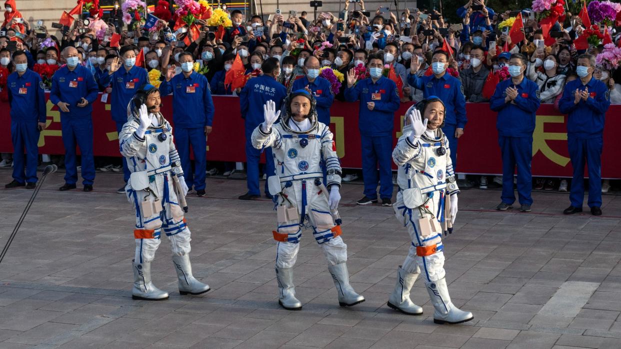  Three astronauts in white suits smile and wave to a crowd. 