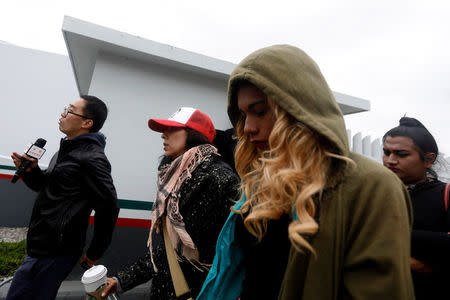 A reporter walks beside members of a caravan of migrants from Central America entering the United States border and customs facility, where they are expected to apply for asylum, in Tijuana, Mexico May 1, 2018. REUTERS/Edgard Garrido