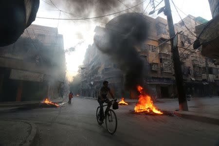 A man rides a bicycle past burning tyres, which activists said are used to create smoke cover from warplanes, in Aleppo, Syria August 1, 2016. REUTERS/Abdalrhman Ismail