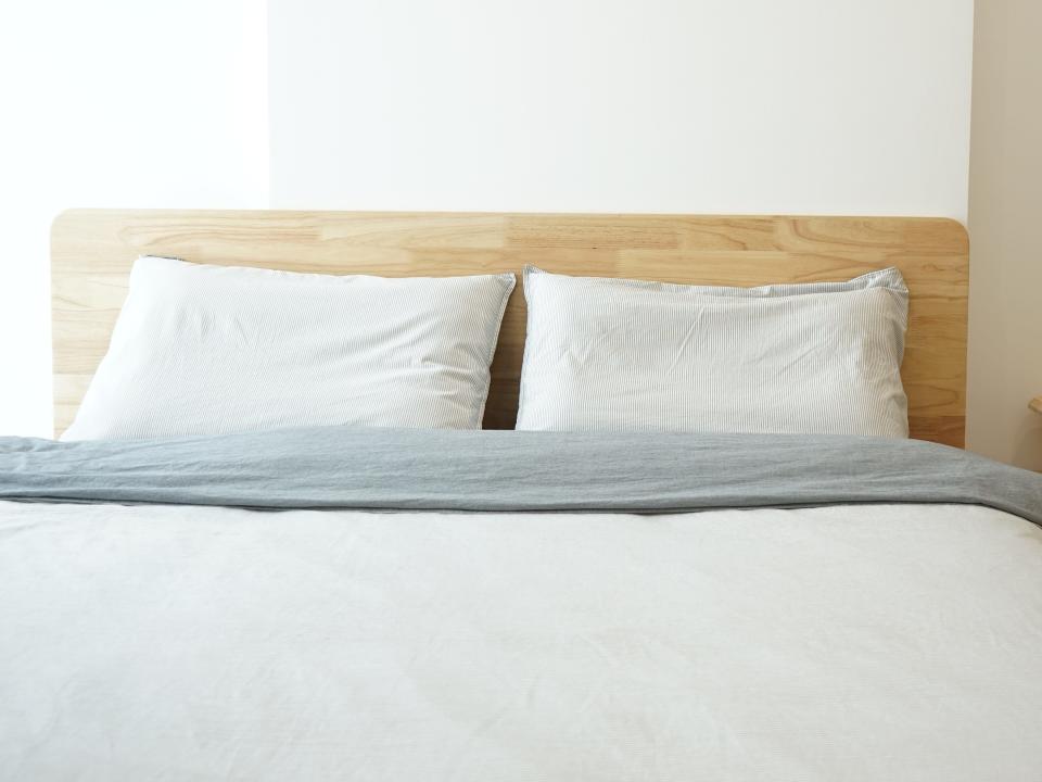 Bed with wooden headboard, white pillows, and white sheets with wooden side table and plant on top