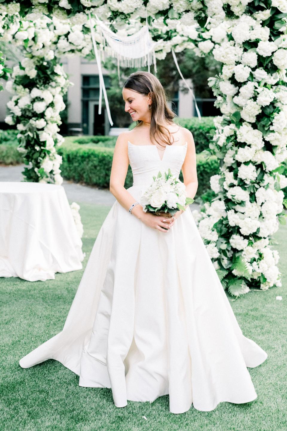 A bride holds a bouquet in front of an oversized floral archway.