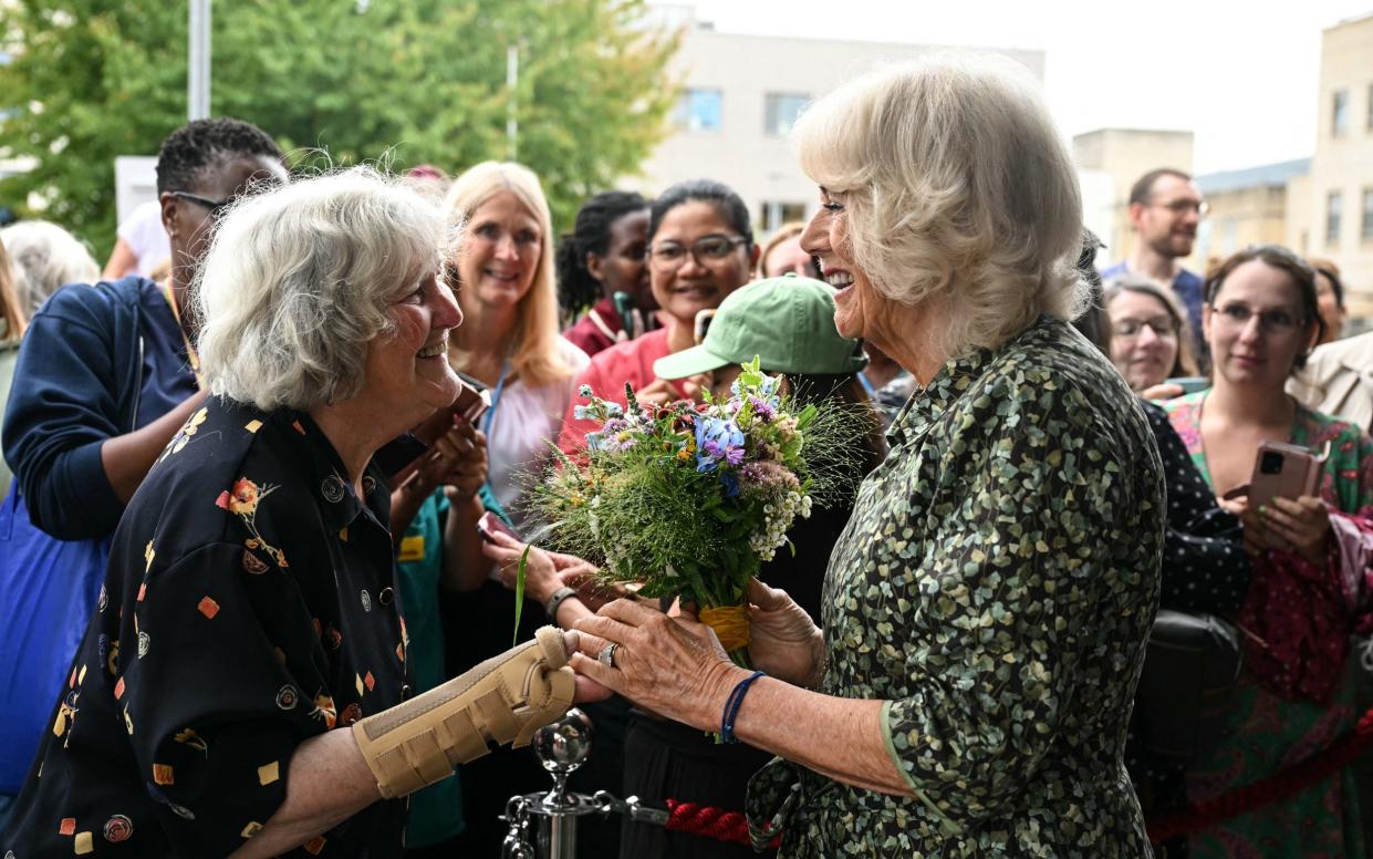 Queen Camilla smiles as she receives a bouquet from an woman of a similar age