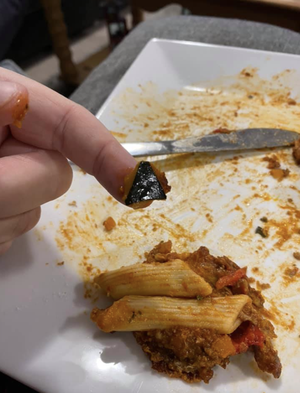 A black object is displayed on a person's finger above a plate with pasta on it.