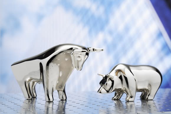 Small chrome bull and bear statues facing one another.