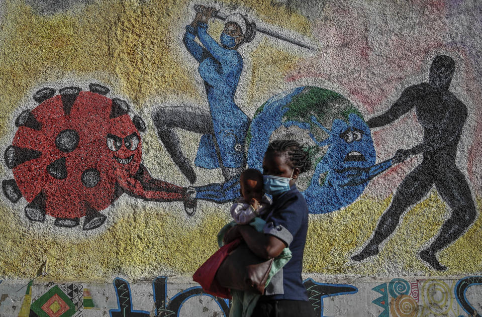 FILE - A woman and child walk past an informational mural portraying the global battle against the coronavirus, on a street in Kericho, Kenya on Jan. 26, 2022. The World Health Organization said Thursday, April 14, 2022 that the number of coronavirus cases and deaths in Africa have dropped to their lowest levels since the pandemic began, marking the longest decline yet seen in the disease. (AP Photo/Brian Inganga, File)