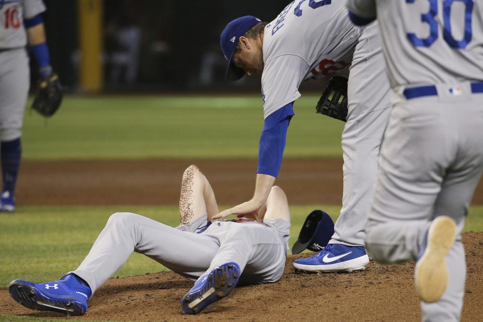 Los Angeles Dodgers relief pitcher Dustin May, left, is comforted by Dodgers' David Freese, second from right, as manager Dave Roberts (30) runs on the field during the fourth inning of a baseball game, after May was hit by a batted ball from Arizona Diamondbacks' Jake Lamb Sunday, Sept. 1, 2019, in Phoenix. (AP Photo/Ross D. Franklin)