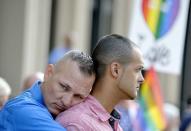 Dwayne D. Beefe-Franqui (L) of Pensacola, Florida, holds on to his husband Jonathan as they stand on the front steps of the federal building waving a rainbow flag in protest of Rowan County clerk Kim Davis' arrival to attend a contempt of court hearing for her refusal to issue marriage certificates to same-sex couples, at the United States District Court in Ashland, Kentucky September 3, 2015. REUTERS/Chris Tilley