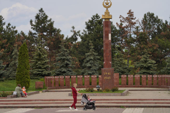 A woman with a child in a stroller walks past a Soviet-era monument marked 1941-1945.