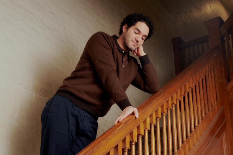 Benny Safdie stands on a stairway and leans against the railing.