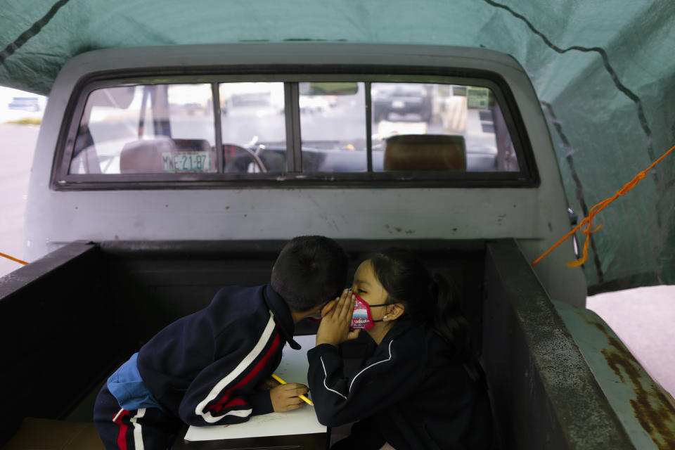 Paulina Mariano Ortiz, 7, whispers to her brother Axel, 5, in a pick-up truck bed repurposed as an educational space on the southern edge of Mexico City, Friday, Sept. 4, 2020. Concerned about the educational difficulties facing school-age children during the coronavirus pandemic, a couple who runs "Tortillerias La Abuela," or Grandma's Tortilla Shop, adapted several spaces outside their locale to provide instruction and digital access to neighborhood children who don't have internet or TV service at home, a project which has attracted donations and a waiting list of students. (AP Photo/Rebecca Blackwell)