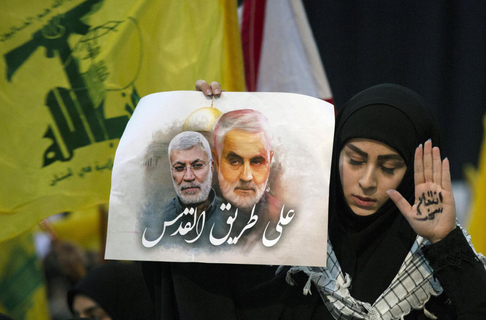 A supporter of Hezbollah leader Sayyed Hassan Nasrallah wears the words "powerful revenge" on her hand, ahead of the leader's televised speech in a southern suburb of Beirut, Lebanon, Sunday, Jan. 5, 2020 following the U.S. airstrike in Iraq that killed Iranian Revolutionary Guard Gen. Qassem Soleimani. The placard in her other hand depicts Soleimaini and Iraq's Popular Mobilization forces commander Abu Mahdi al-Muhandis, who was also killed in the strike. Arabic on placard reads: "On the road to Jerusalem." (AP Photo/Maya Alleruzzo)