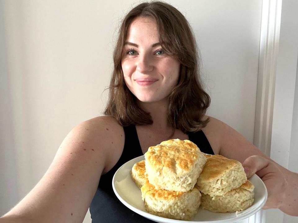 A woman takes a selfie while holding a plate with a pile of biscuits on it.