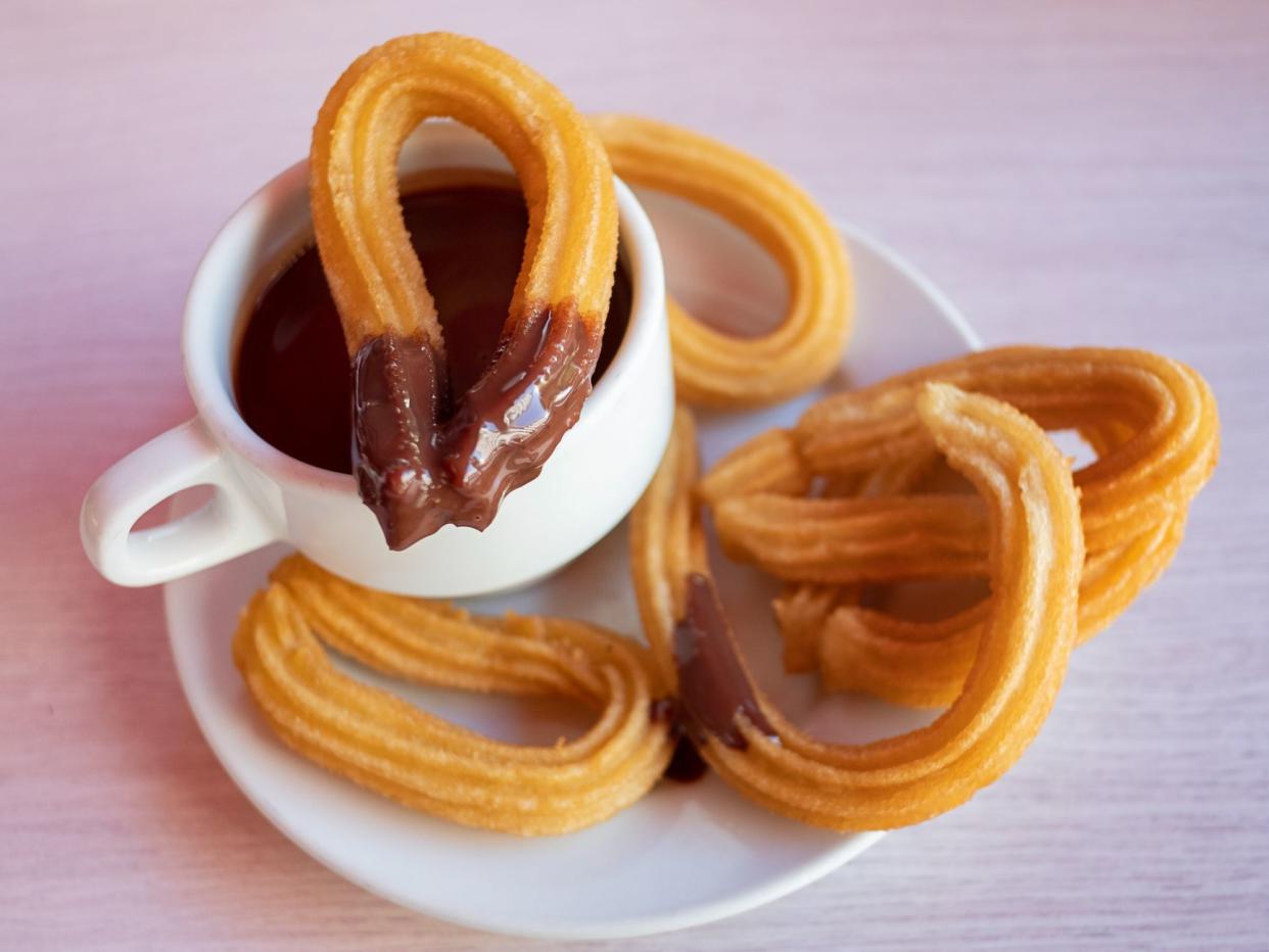 Churros con chocolate caliente, a traditional Spanish street food, a sweet treat consisting of a cup of thick hot chocolate drink and crispy, long and curly fried-dough pastry served aside for dipping.