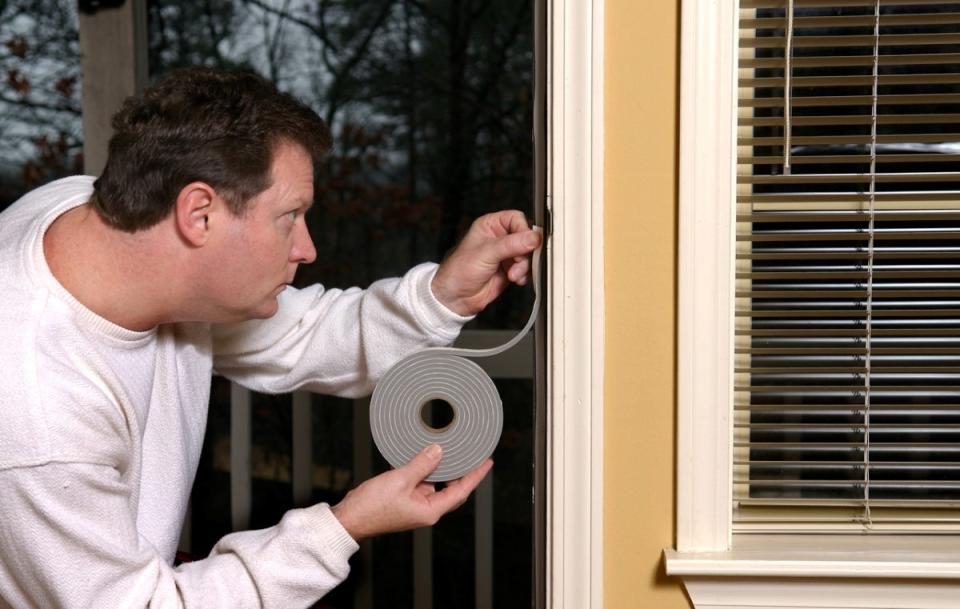 Man weather stripping an exterior door on his home with a roll of weatherstripping tape.