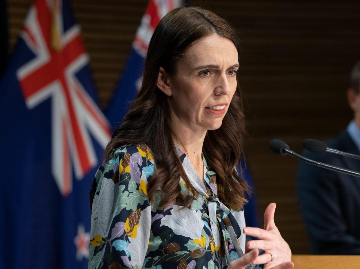 New Zealand Prime Minister Jacinda Ardern at a lectern with flag and a man in the background