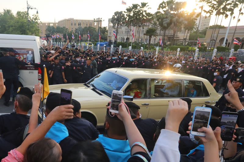 The royal motorcade carrying Thailand's Queen Suthida and Prince Dipangkorn drives past a group of anti-government demonstrators in front of Government House in Bangkok