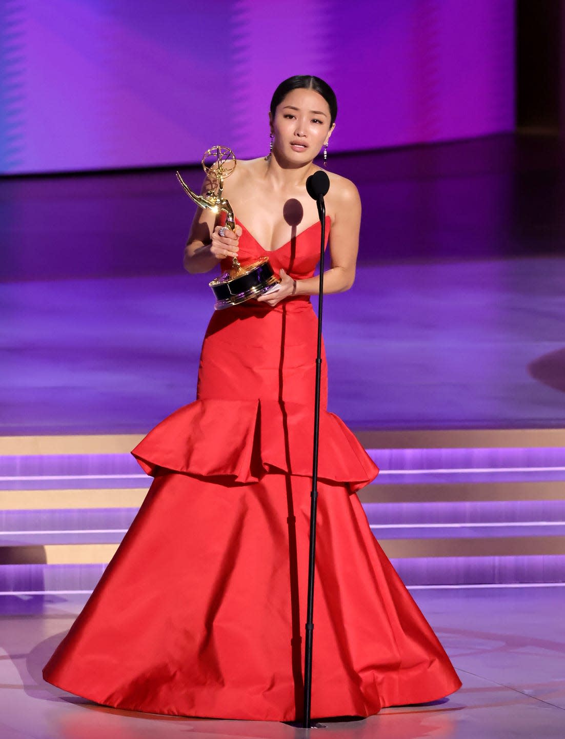 anna sawai holding an emmy trophy in her hands as she speaks at a microphone