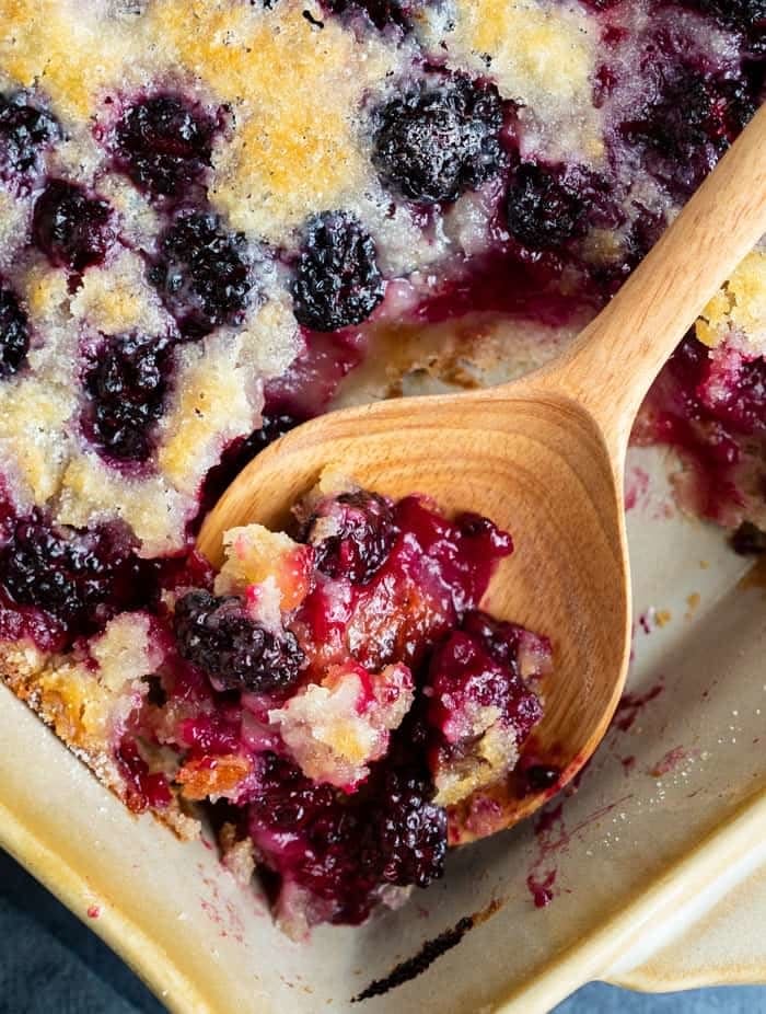 A close-up of a scoop of blackberry cobbler on a wooden spoon.