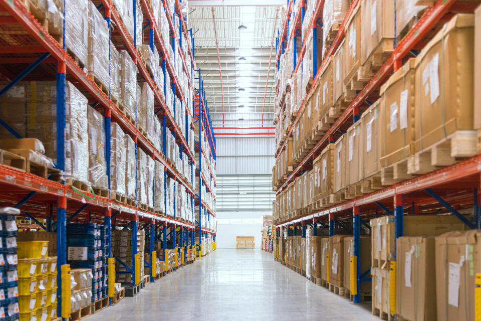 Warehouse aisle with tall shelves filled with boxes, pallets, and packages, representing storage and logistics in a work and money context