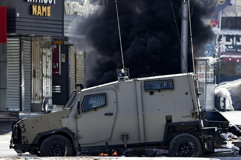 Un vehículo del ejército israelí circula junto a unos neumáticos en llamas a la entrada de Yenín, en la Cisjordania ocupada, durante una operación el 13 de junio de 2024 (Zain Jaafar)