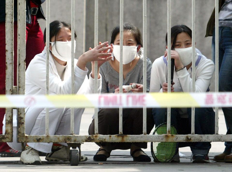 Three women crouch inside the closed gate of the People's Hospital of Peking University in Beijing Friday April 25, 2003.