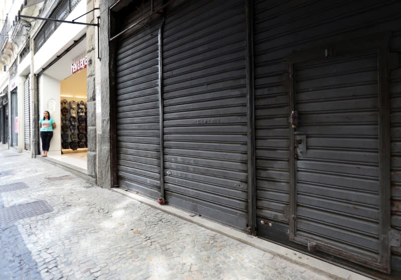 A vendor stands next to a partially closed shop after authorities announced measures to curb the spread of coronavirus disease (COVID-19), in downtown of Rio de Janeiro