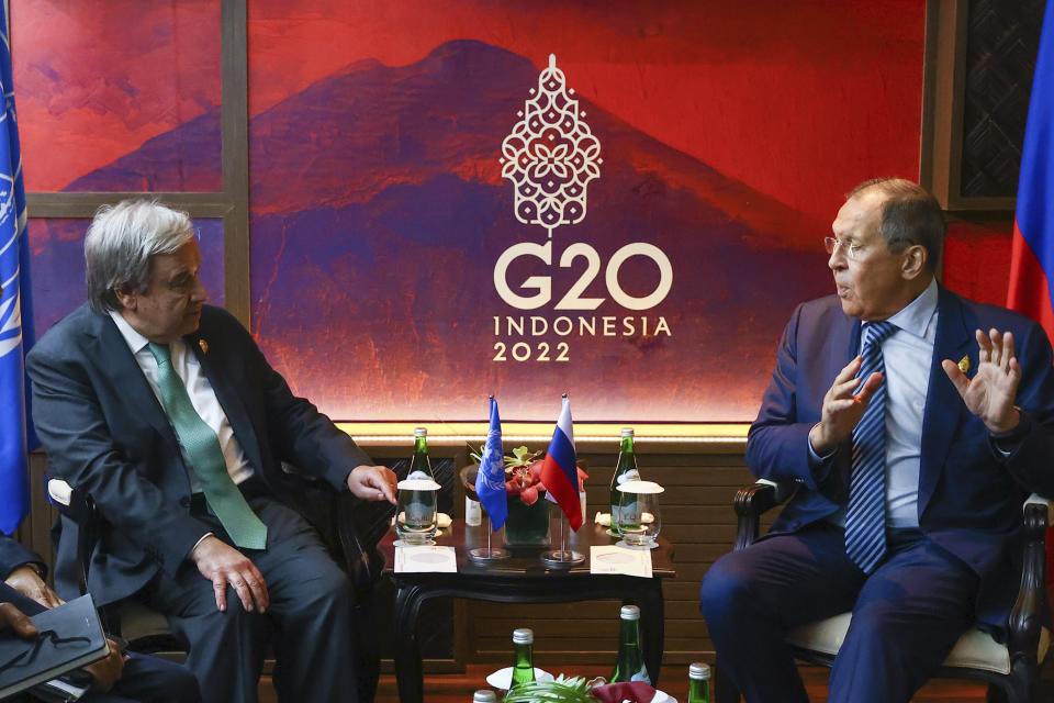 Guterres and Lavrov are seated in chairs between a side table, on which rest two small flags, two empty glasses and a few bottles of mineral water, in front of a red backdrop that reads: G20 Indonesia 2022.