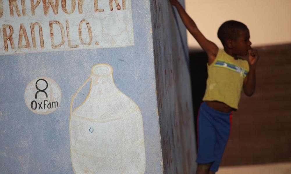 Haitian boy stands next to Oxfam sign