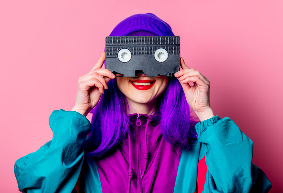 Stylish white girl with purple hair, 80s tracksuit hold video tape on pink background