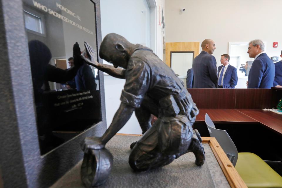 A small statue honoring veterans is seen in the foreground as Massachusetts Veterans Services Secretary Jon Santiago speaks with Rep. Tony Cabral during a visit to the Veterans Transition House in New Bedford.