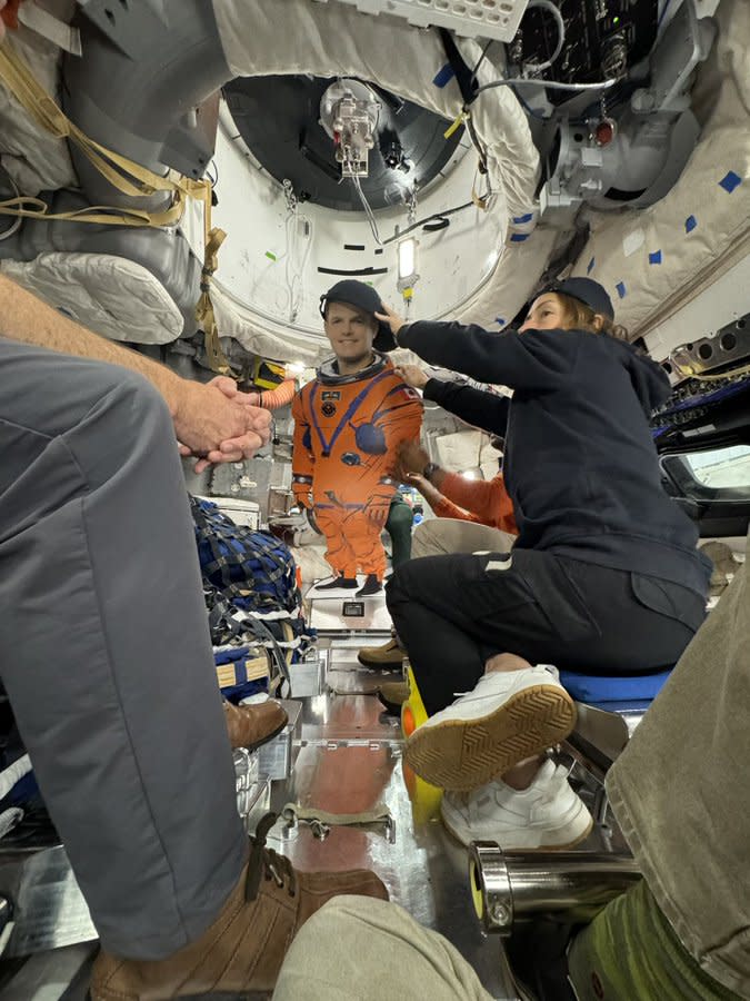 astronauts sitting in a spacecraft holding up a cardboard cutout of a spacesuited astronaut