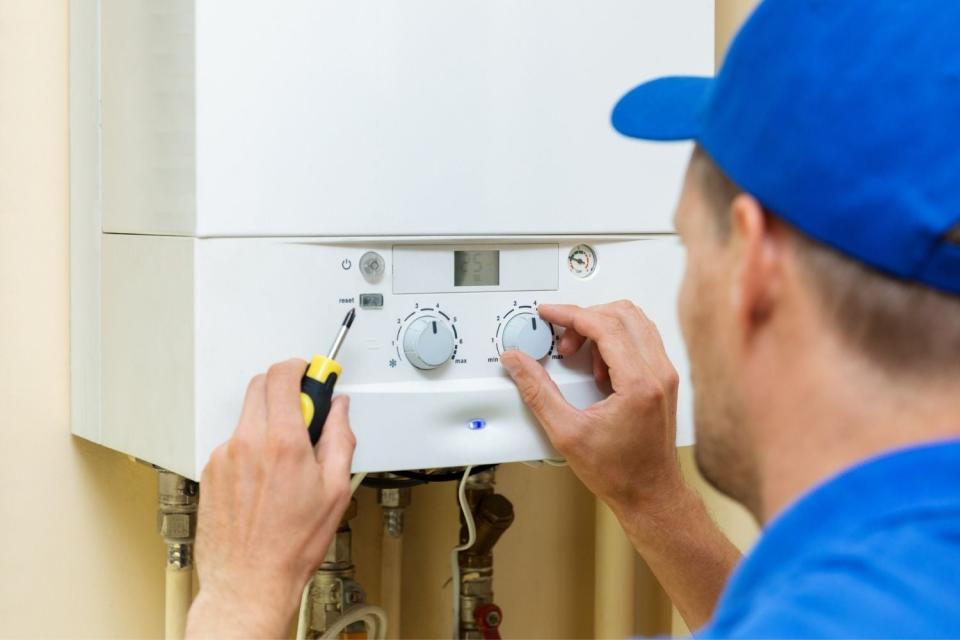 A worker in a blue cap turns a dial on a tankless water heater. 